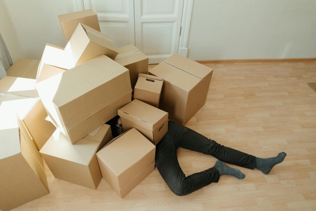 Persona agotada bajo un montón de cajas de cartón en el suelo, simbolizando el estrés y la fatiga de una mudanza