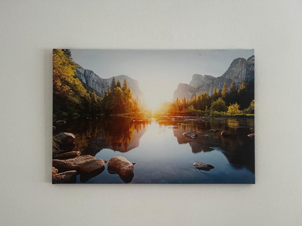 Fotografía de gran angular del sol poniente sobre el río Merced, reflejando el brillo dorado en la superficie del agua. El río fluye a través de una densa arboleda de pinos y está rodeado por grandes rocas. Al fondo, las imponentes paredes de granito de El Capitán y Cathedral Rocks se elevan hacia un cielo brillante y despejado
