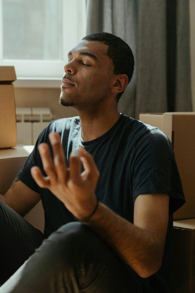 Hombre joven practicando meditación entre cajas de mudanza para reducir el estrés