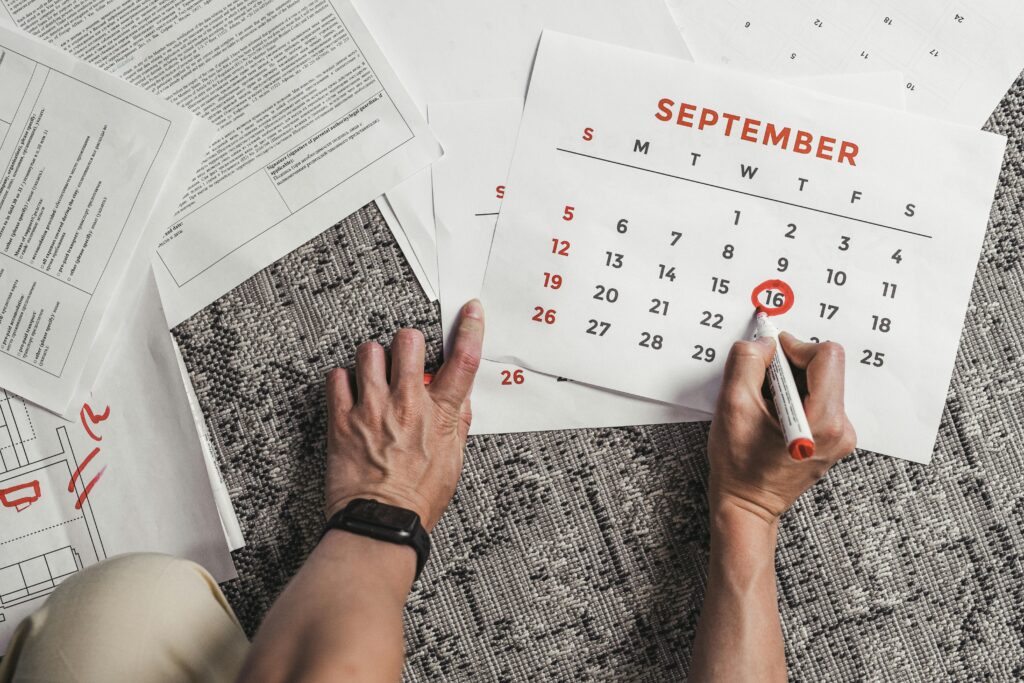 Manos señalando y marcando el 16 de septiembre en un calendario sobre la mesa, junto a documentos