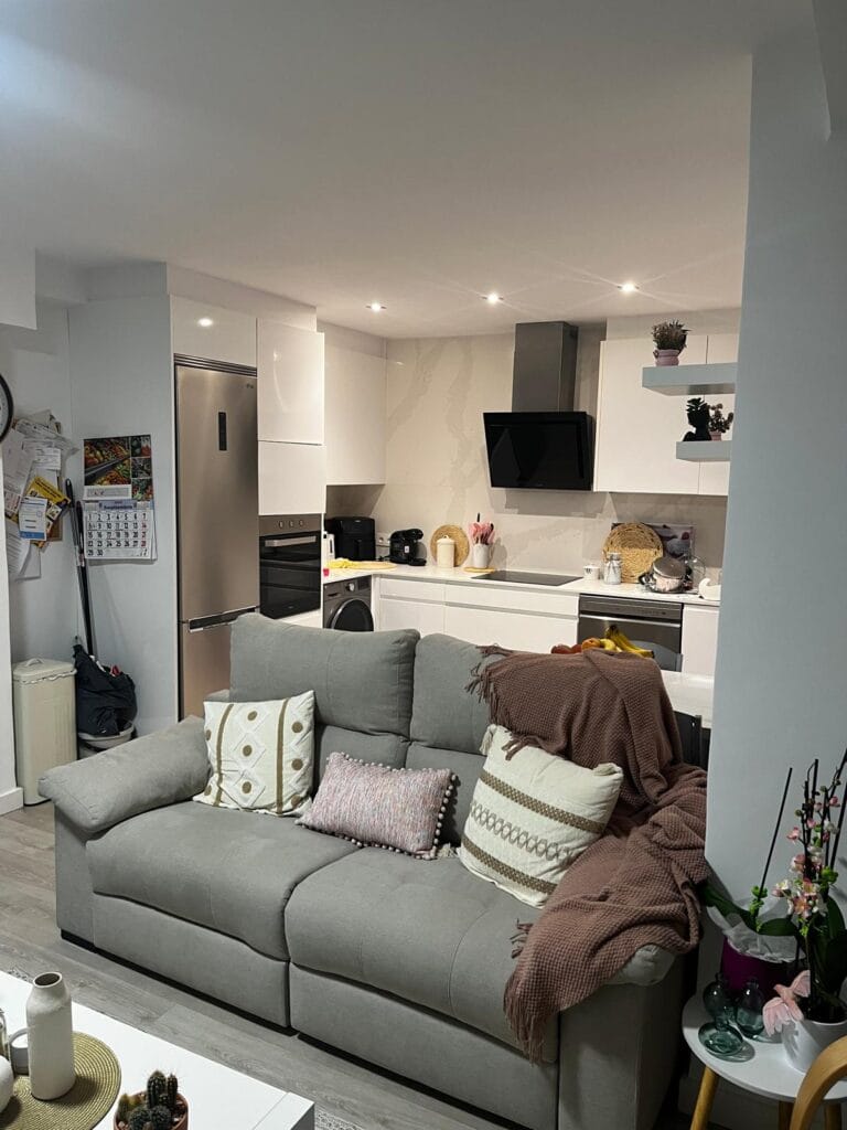 Sala y cocina moderna integradas en tonos blancos y grises Sala y cocina integradas con diseño moderno en tonos neutros, sofá gris con cojines decorativos y cocina blanca minimalista con electrodomésticos de acero inoxidable