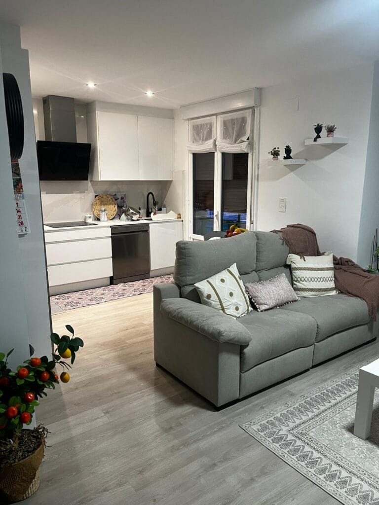 Cocina abierta al salón con decoración moderna y luminosa Cocina blanca abierta al salón con sofá gris y decoración nórdica, iluminación empotrada y ventanales que aportan luz natural